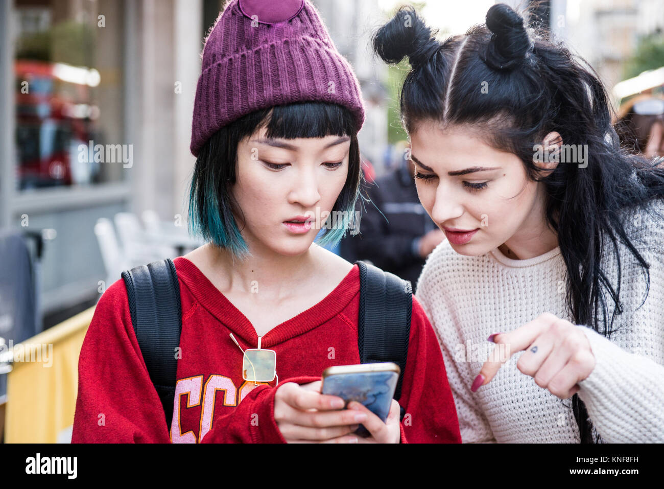 Due giovani donne eleganti guardando smartphone su una strada di città Foto Stock