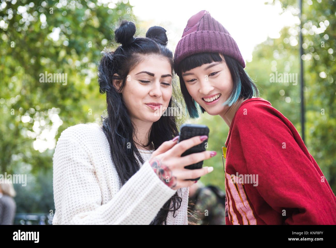 Due giovani donne eleganti guardando lo smartphone nel parco della città Foto Stock