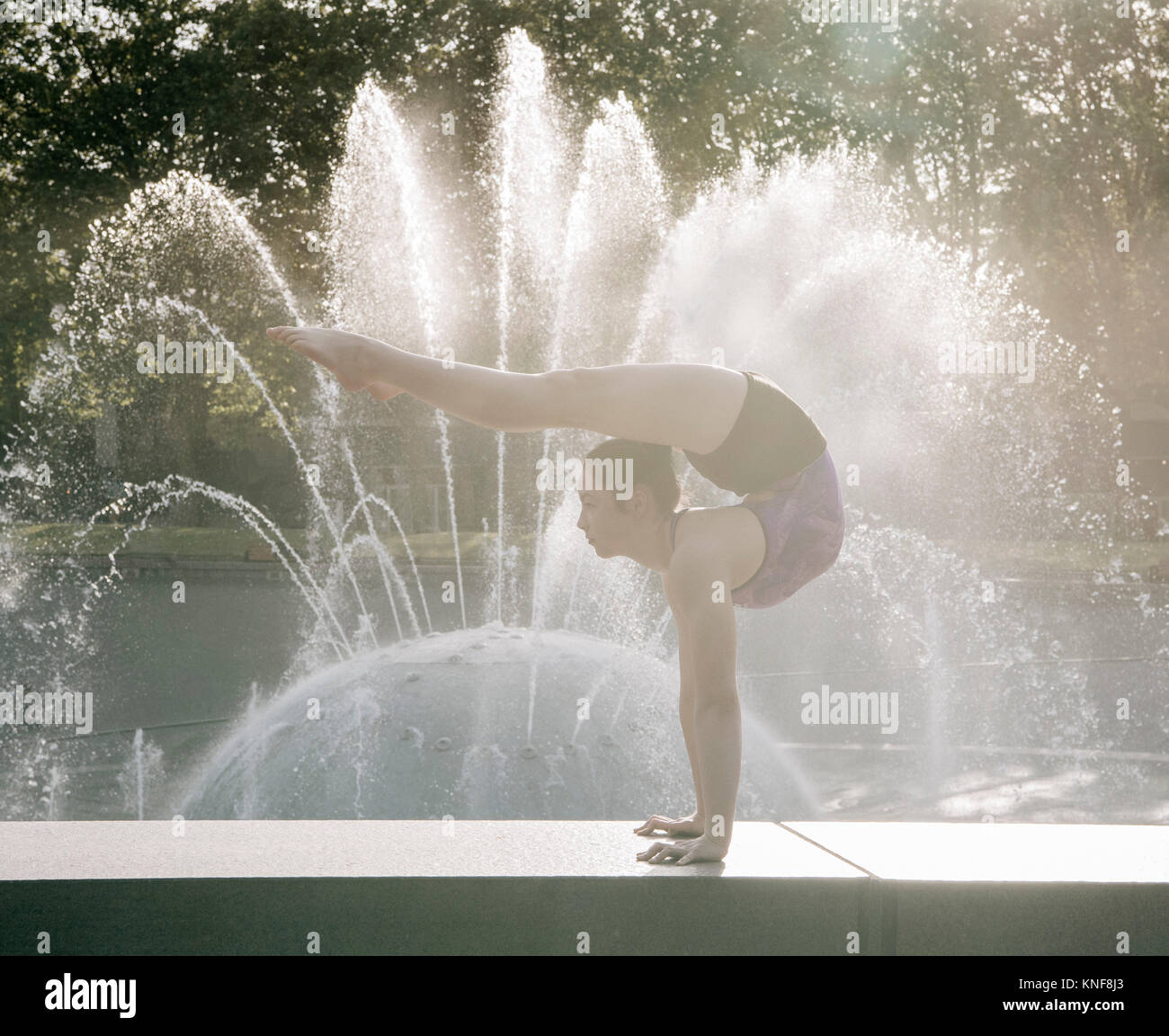 Ragazza adolescente accanto alla fontana, equilibratura su mani in posizione di yoga Foto Stock