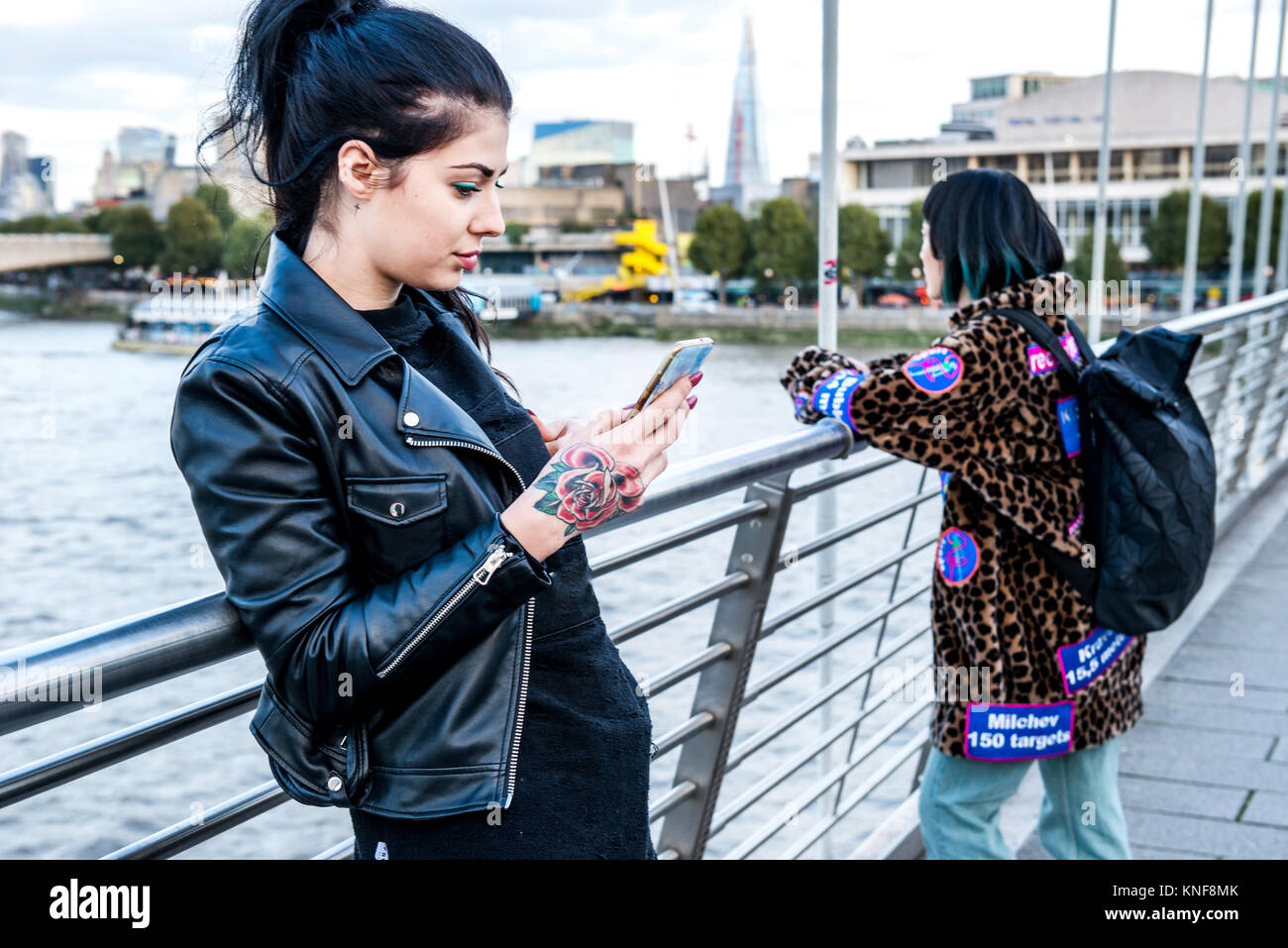Giovane donna guardando smartphone con amico guardando fuori dalla passerella del millennio, London, Regno Unito Foto Stock