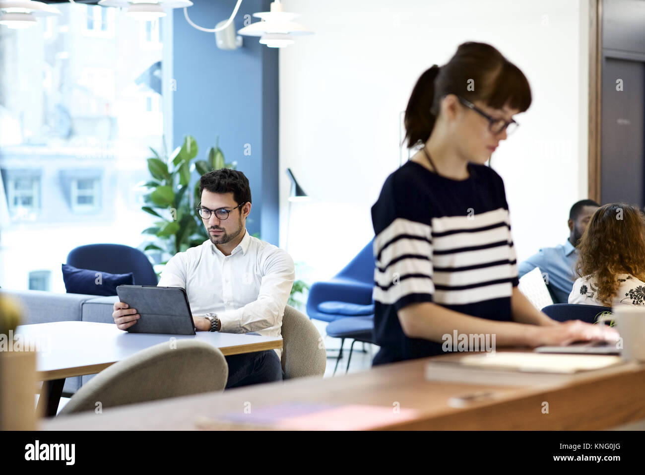 Imprenditore informale sat in un ufficio utilizzando una tavoletta mobile device che indossa gli occhiali da lettura Foto Stock