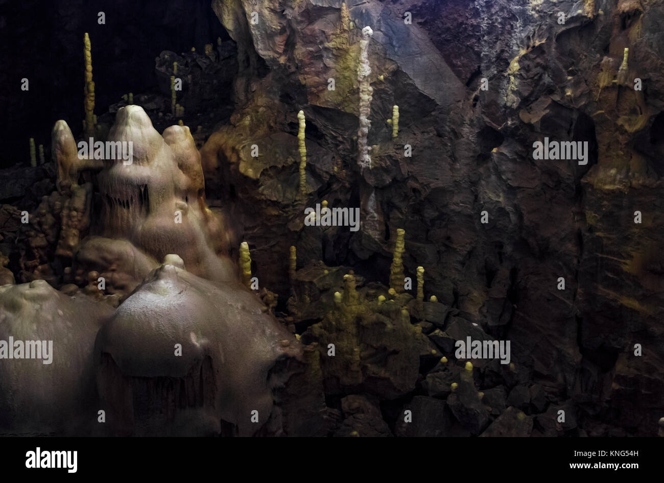 Grotta con colorate pareti ruvide e stalattiti e stalagmiti illuminato da dietro Foto Stock