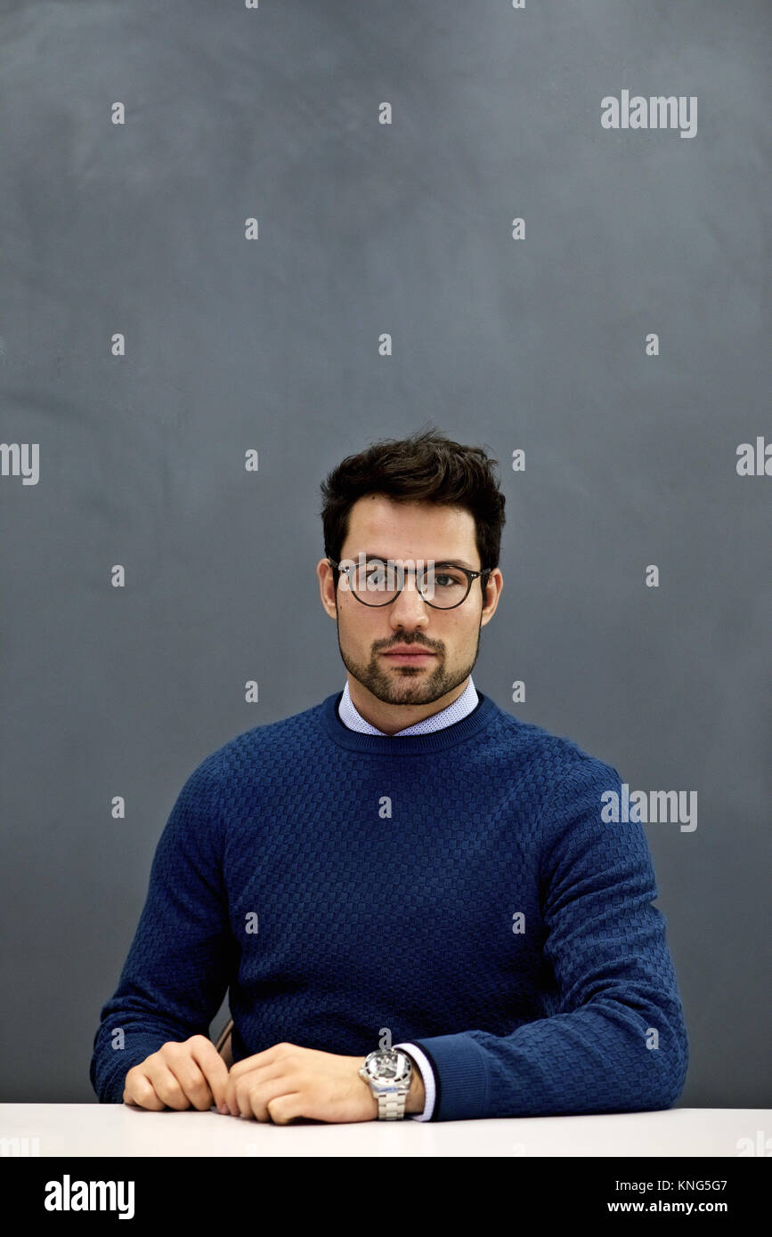 Ritratto di un orgoglioso e determinata giovane imprenditore caucasico seduta con un semplice sfondo grigio e lo spazio per la copia Foto Stock