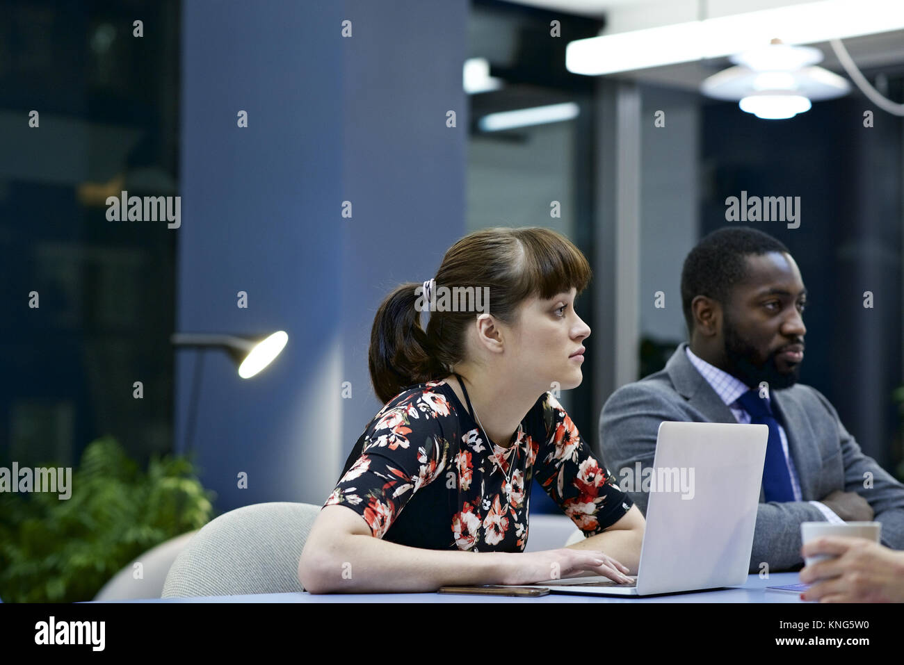 Caucasian business donna con un computer portatile e maschio nero collega in una riunione del team in un ufficio contemporaneo Foto Stock