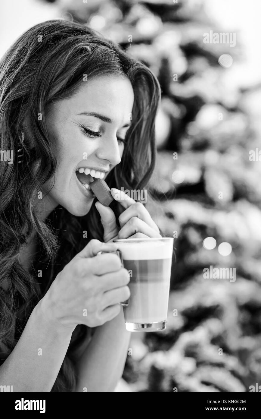 Ritratto di profilo di felice giovane donna mangiando caramelle con il latte macchiato vicino albero di natale Foto Stock Ritratto di profilo di felice giovane donna mangiando caramelle con il latte macchiato vicino albero di natale Foto Stock