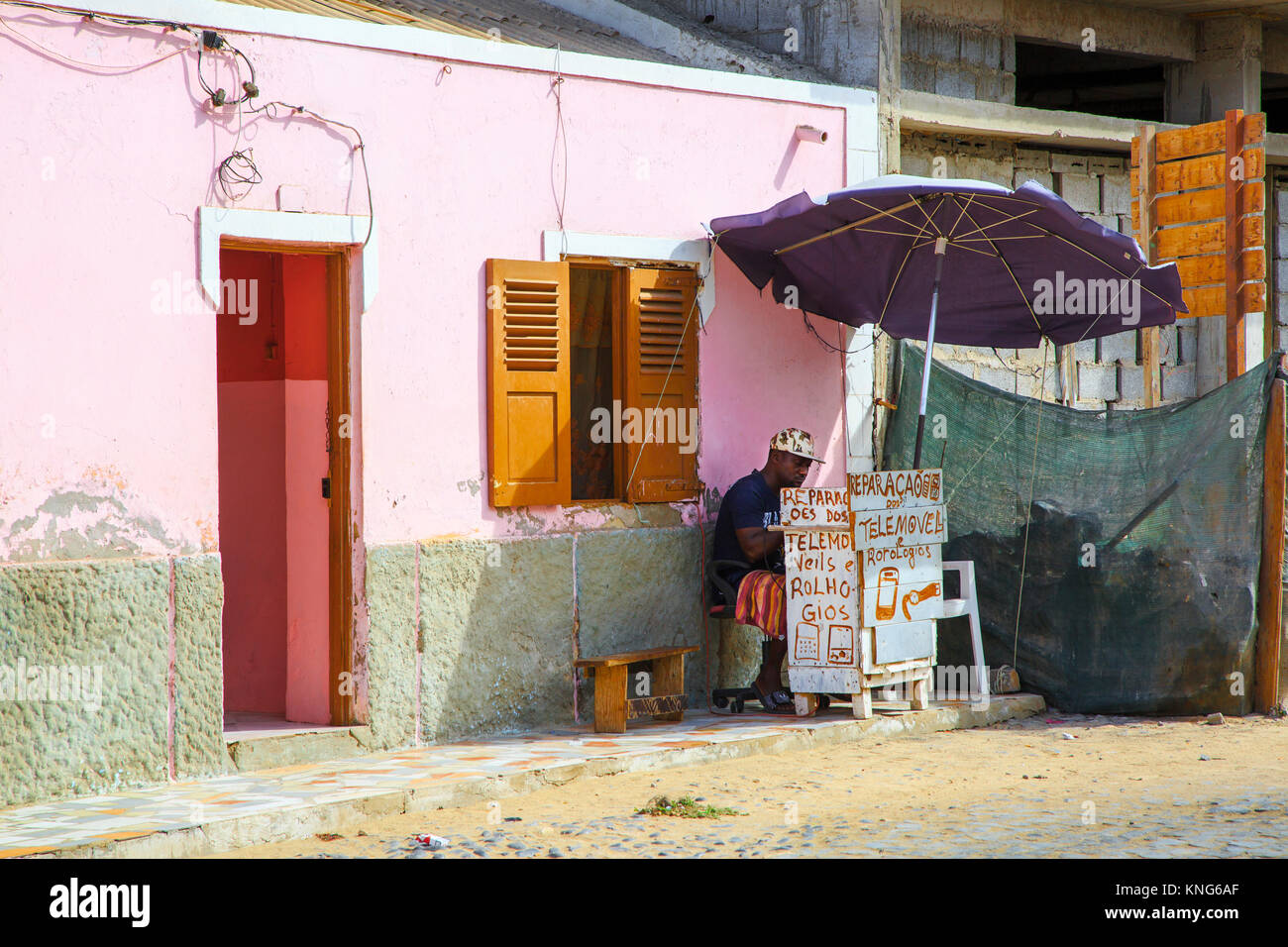 Uomo che ripara orologi e telefoni cellulari da un piccolo box in una strada secondaria di Santa Maria, Isola di Sal Capo Verde Foto Stock