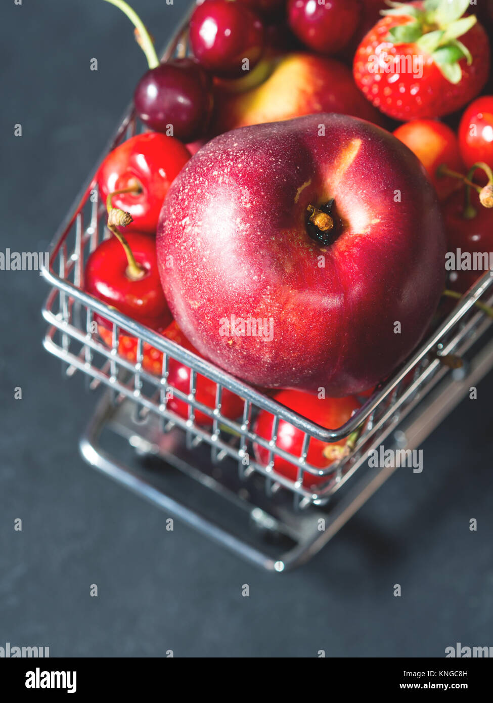 Rosso fresco frutta e bacche - di ciliegie, di pesche e di fragole - in carrello per supermercati vassoio su sfondo nero. Spazio di copia Foto Stock
