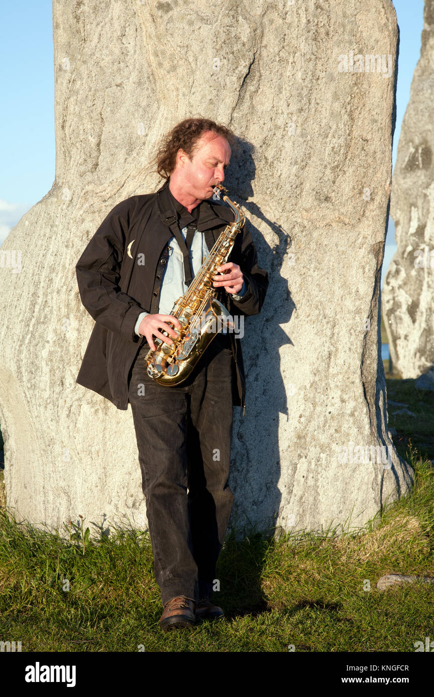 Il sassofonista giocando a Callanish standing stones, isola di Lewis, durante il solstizio d'estate Foto Stock