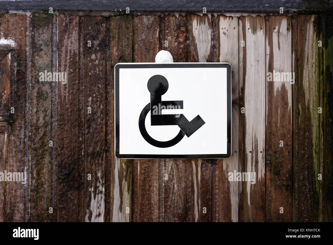 Parcheggio segno di accesso per persone disabili su una tavola di legno parete congelata. Icona di un disabile su sedia a rotelle. Foto Stock