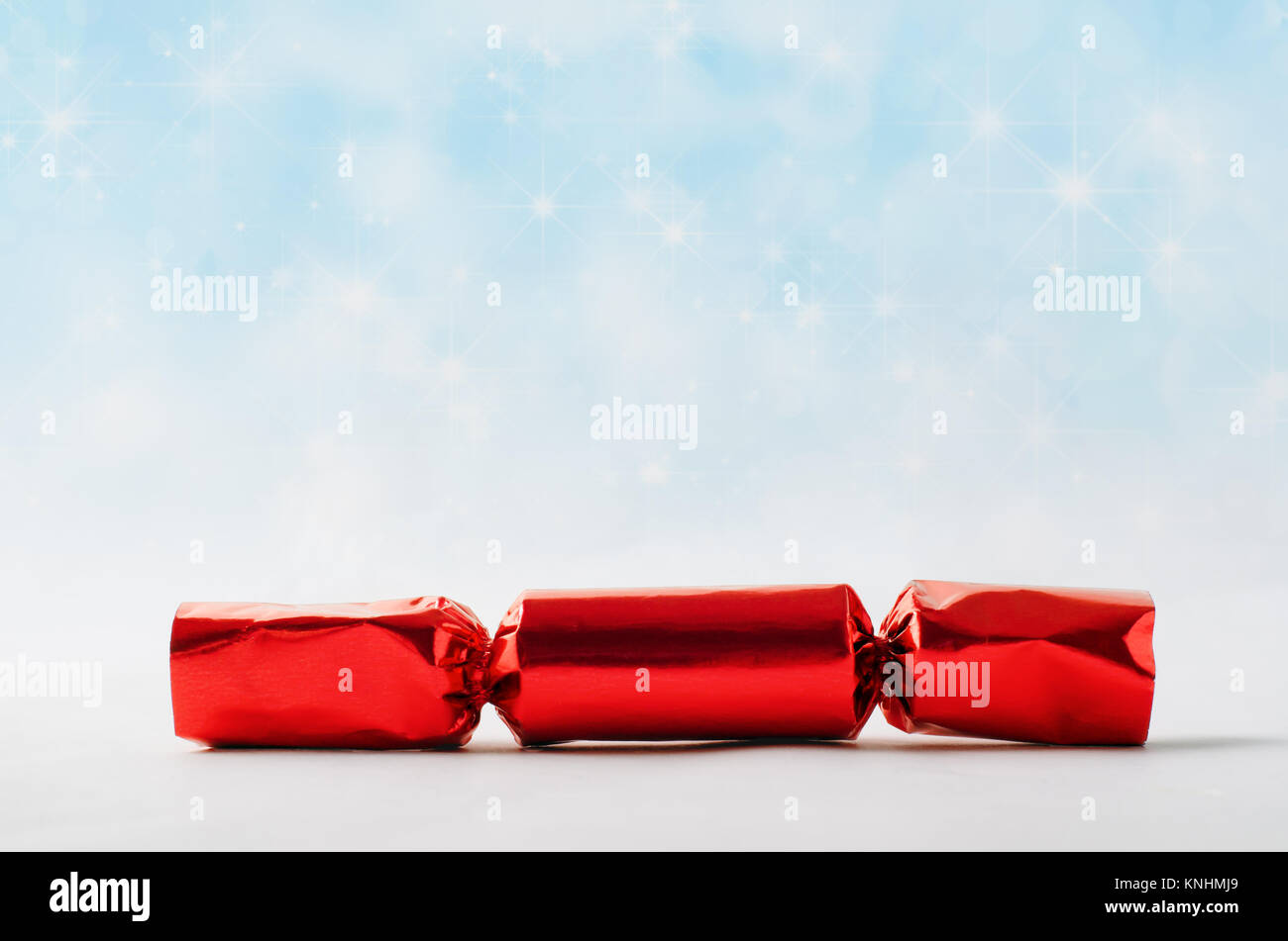 Un singolo foglio rosso Christmas Cracker, contro la luce blu sfondo bokeh di fondo simulando una stella riempito il cielo con la caduta di neve. Foto Stock