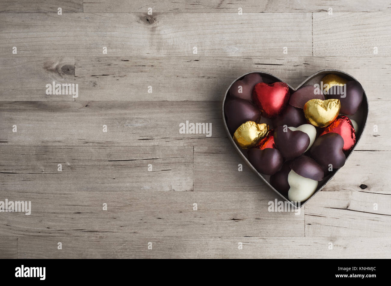 Tettuccio di colpo di cuore aperto a forma di scatola contenente una varietà di Cioccolatini e pralines sui vecchi e usurati luce asse di legno tabella. Foto Stock