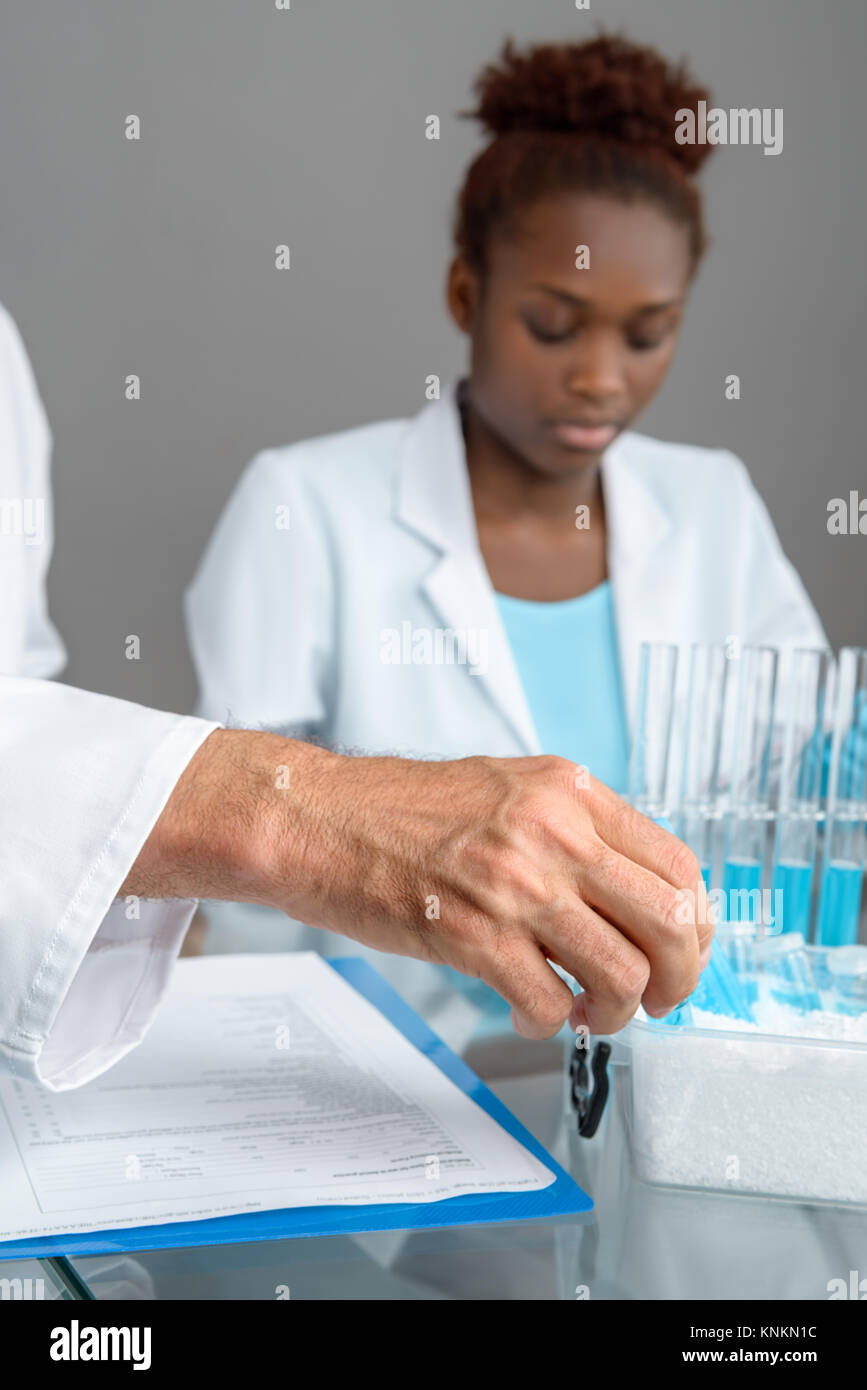 Primo piano su un lato di un maschio senior scientist di prelievo campione scientifico da ice box, lavorando African donna scienziato fuori fuoco, spazio di testo Foto Stock