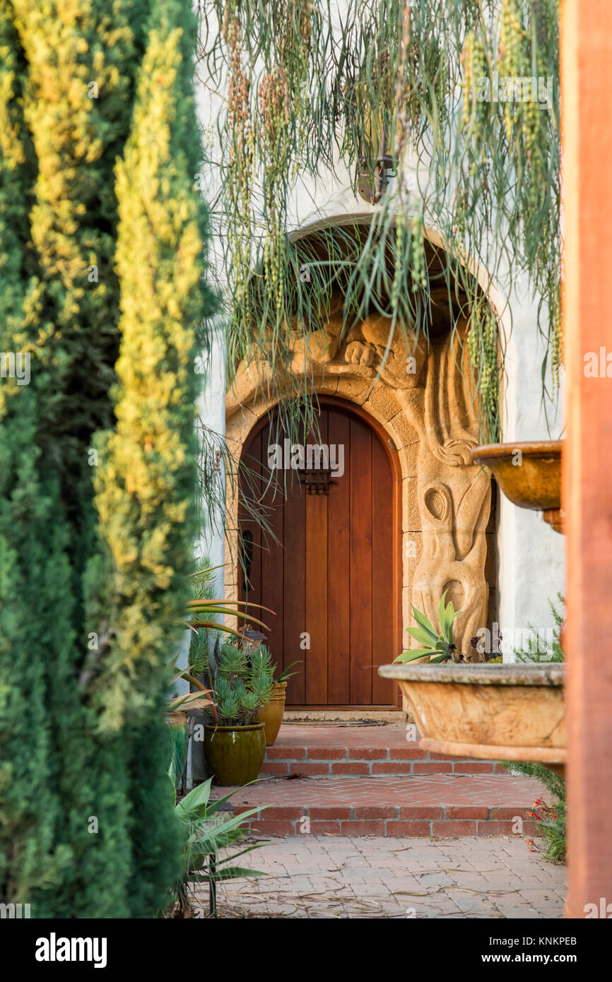 Dettaglio verticale shot architettonico di una pietra arenaria artigianali entrata ad arco con una porta di legno. Mediterraneo spagnolo revival stile della California. Foto Stock
