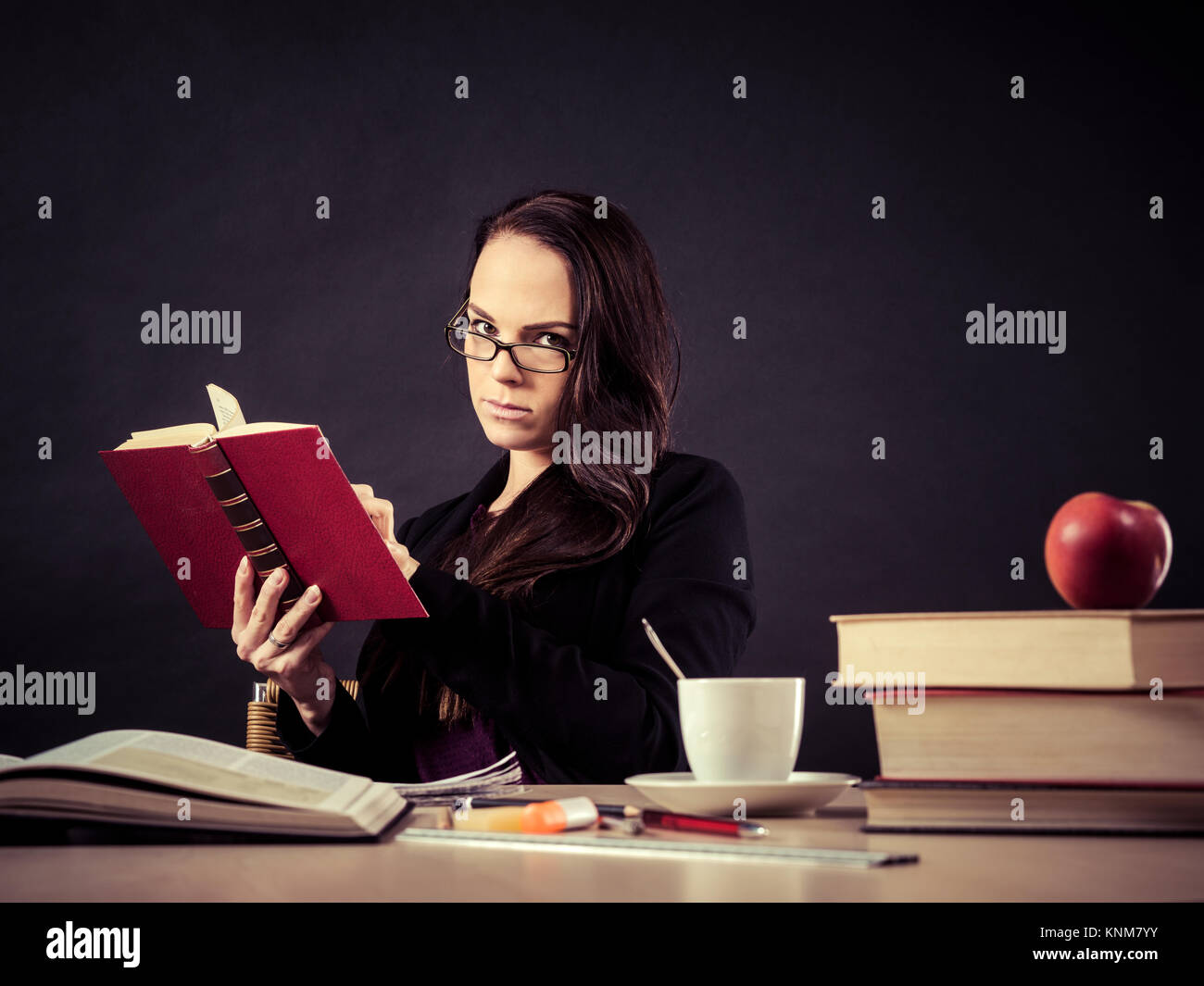 Foto di un maestro nel suo 30's seduti ad una scrivania disordinato di fronte a una grande lavagna la lettura di un libro. Foto Stock