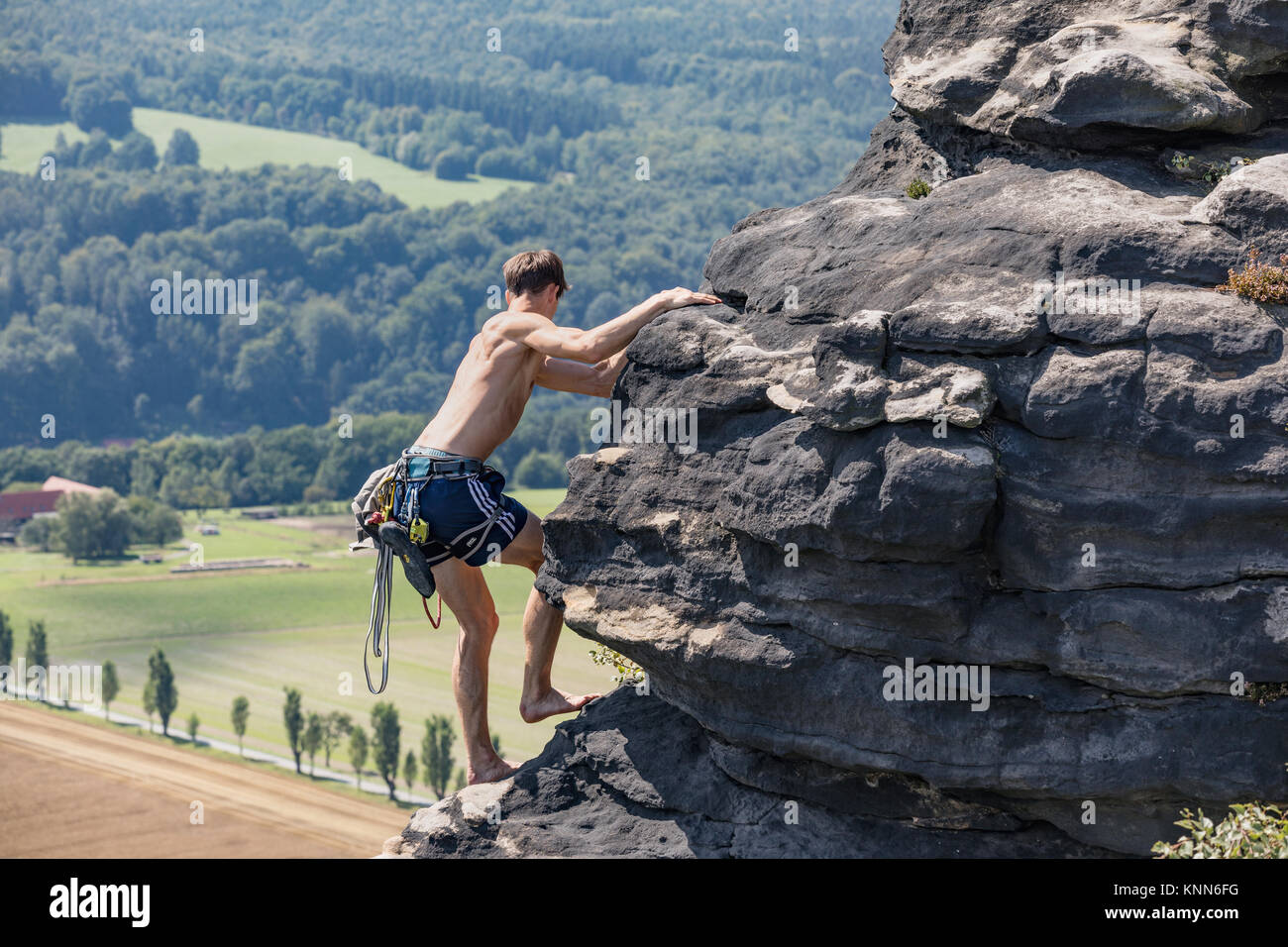 Lilienstein, Germania - 14 agosto 2017. Un giovane scalatore con un corpo muscoloso salite a piedi nudi lungo il bordo di una roccia arenaria. Scalatore in Sassone Swit Foto Stock