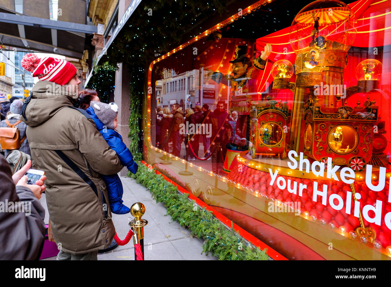 Gente della scena natalizia, padre che tiene in braccio il bambino che guarda la finestra delle vacanze natalizie di Saks Fifth Avenue nel centro di Toronto, Canada. Foto Stock