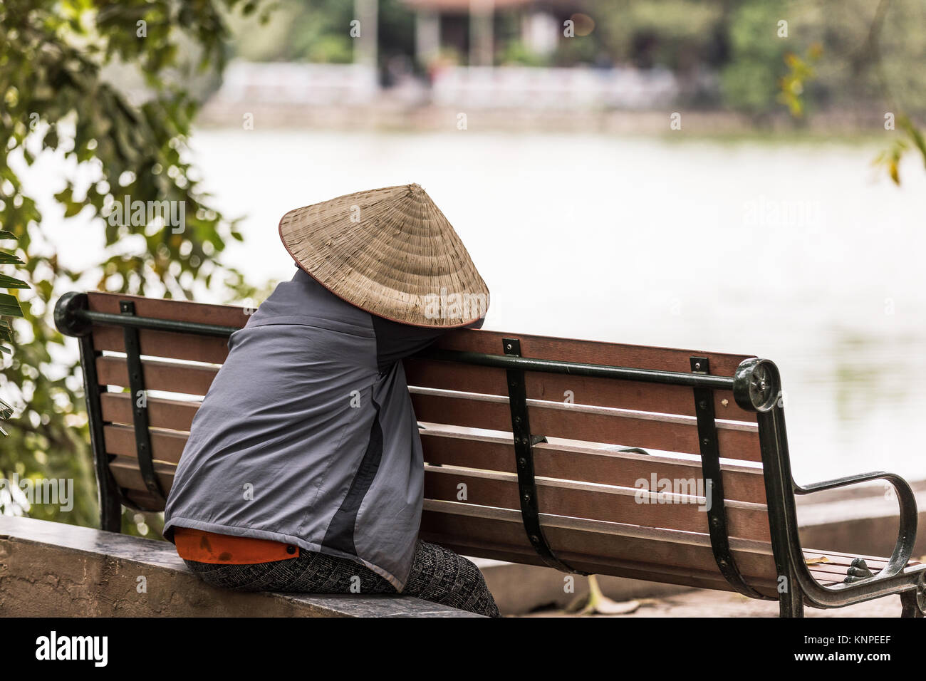 Donna con il tipico vietnamita cappello di bambù in appoggio su una panchina in riva al lago Foto Stock