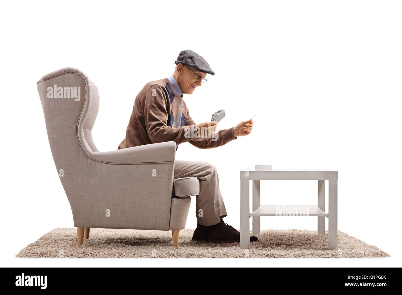 Senior seduto in poltrona a giocare a carte da lui stesso isolato su sfondo bianco Foto Stock
