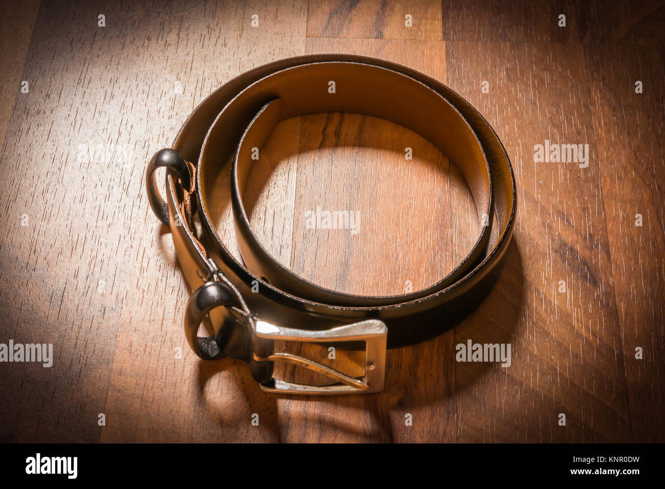 Cinghia in pelle gli uomini vestito arrotolata su pavimento in legno Vignette pavimento Spotlight Foto Stock