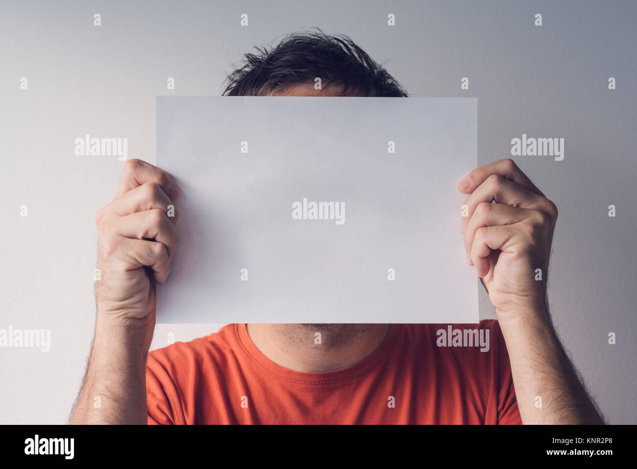 L'uomo nascosto dietro vuoto carta bianca come copia di spazio per un messaggio di testo Foto Stock