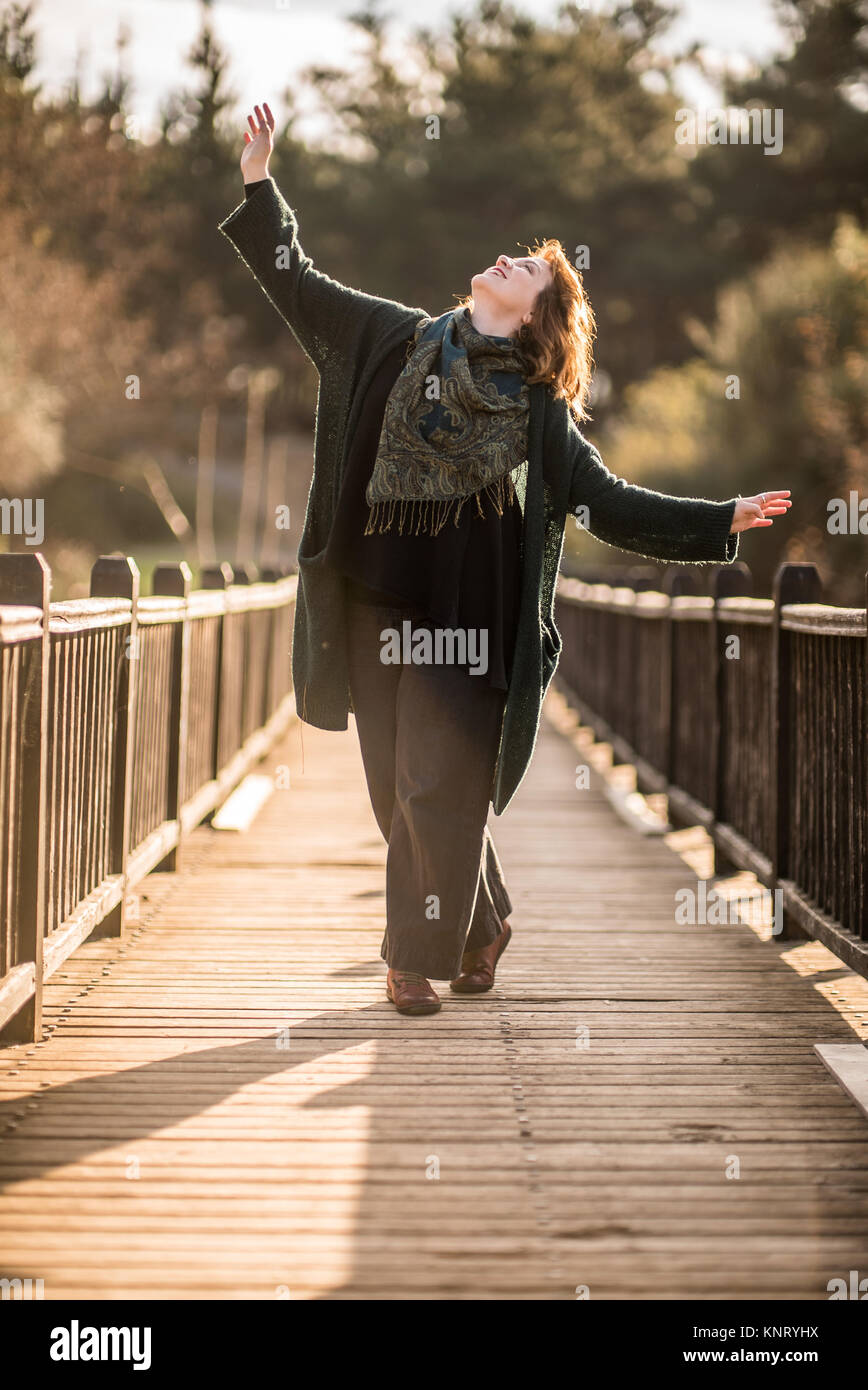 Donna felice in posa su una tavola di legno vecchio ponte nella foresta per godersi la vita Foto Stock