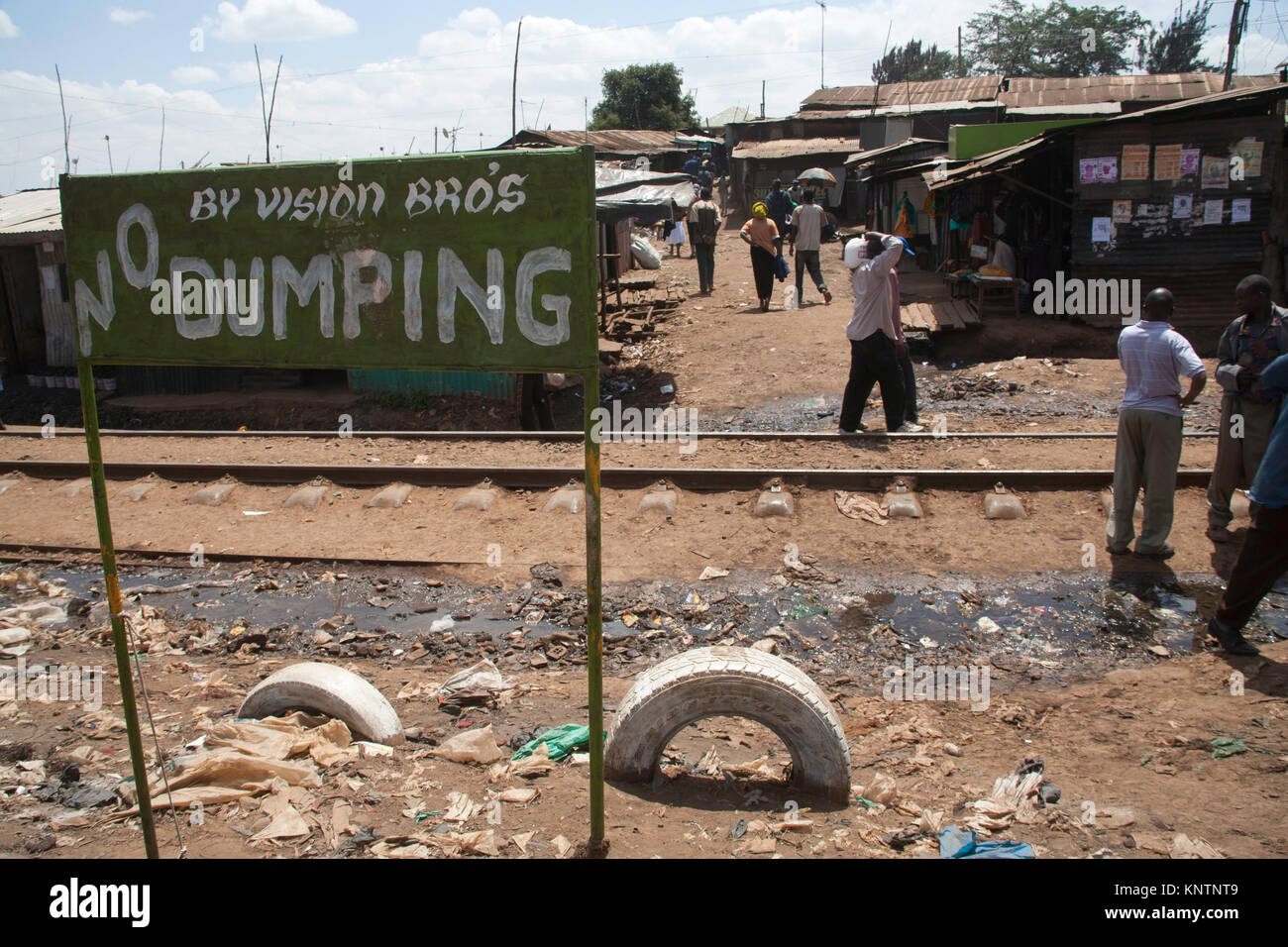 La gente a piedi lungo il binario di Kibera baraccopoli, dietro un segno dicendo no dumping, Nairobi, Kenya, Africa orientale Foto Stock