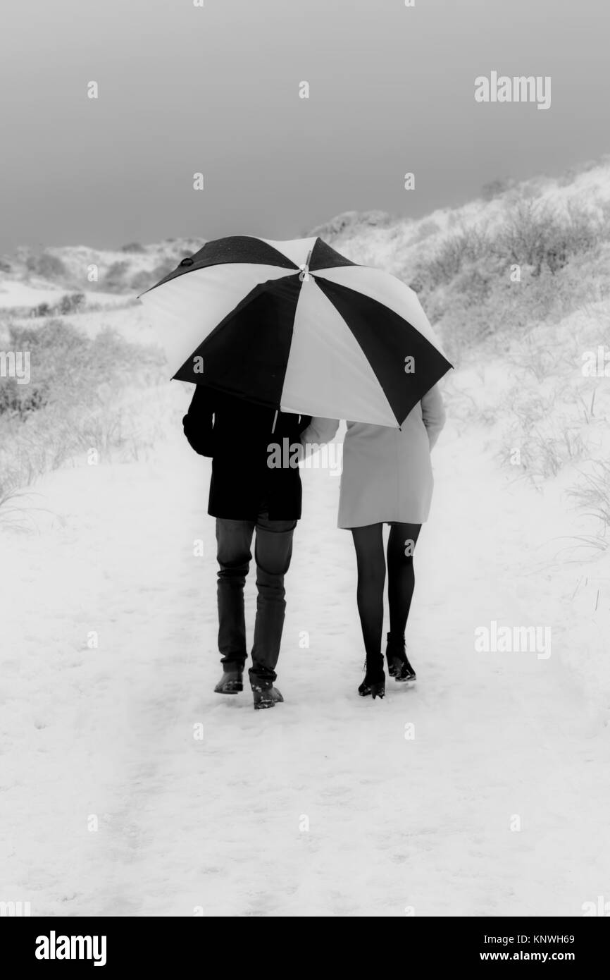 Romantica scena stagionale: una giovane coppia passeggiate nella neve, rifugiandosi sotto un enorme ombrello. Foto Stock