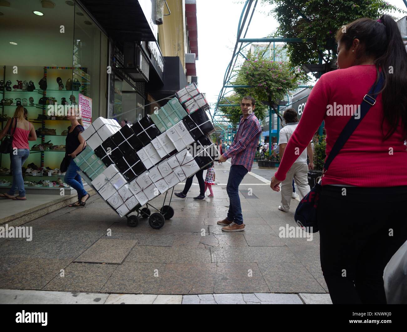 Cordoba, Argentina - 2016: un uomo porta un carrello pieno di scatole di scarpe da un marciapiede occupato in una scarpa negozio al centro della citta'. Foto Stock