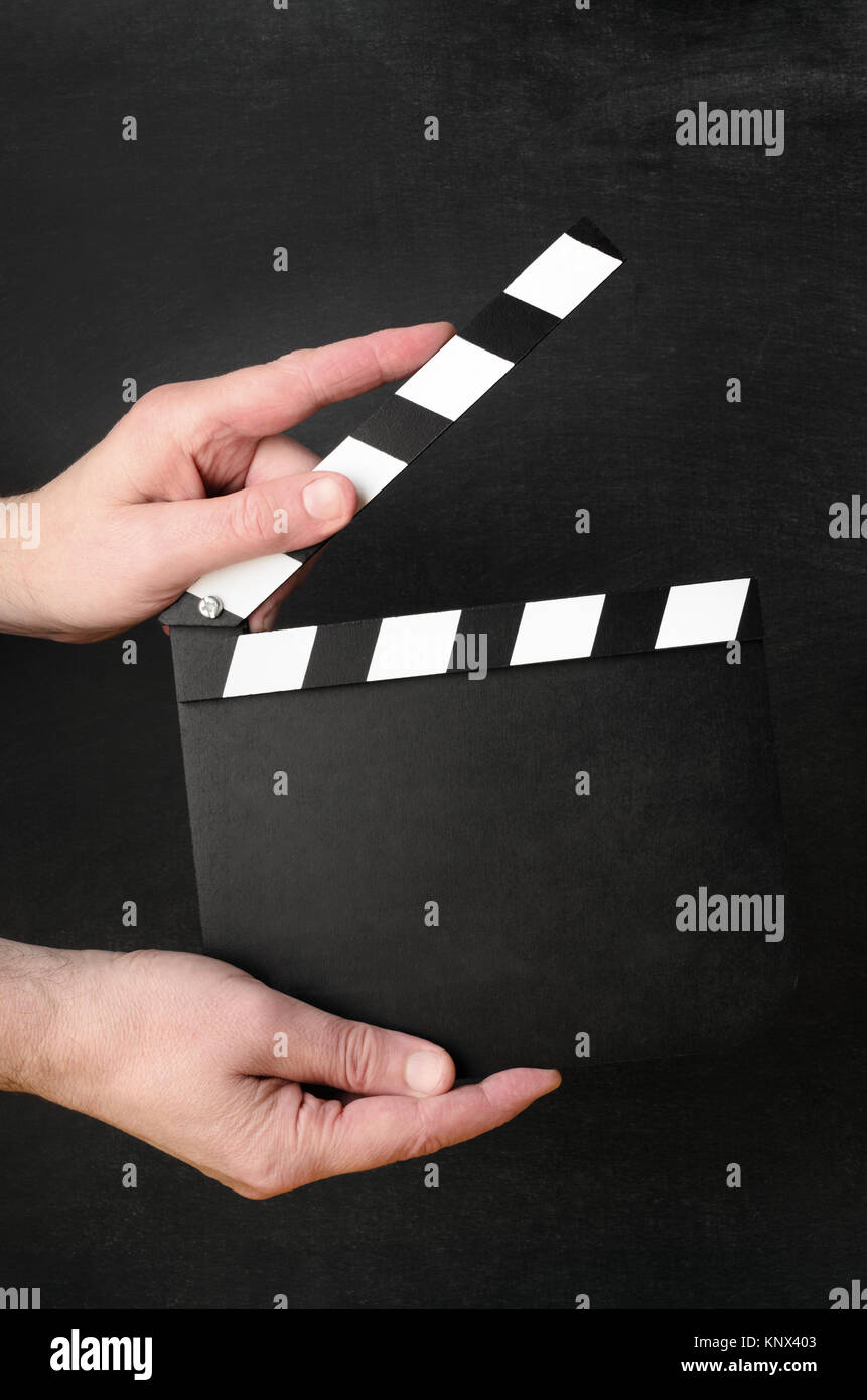 Un fustellato clapperboard tenuto aperto come se attorno alla chiusura a scatto tra le mani di un maschio operative con la lavagna nera dello sfondo. Foto Stock