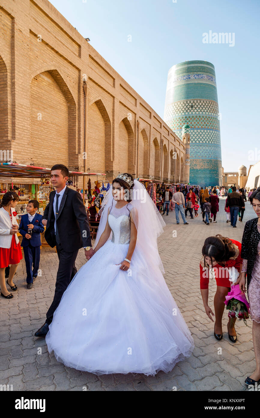 Una giovane coppia uzbeka a piedi attraverso le strade di Khiva dopo esserci sposati, Khiva, Uzbekistan Foto Stock