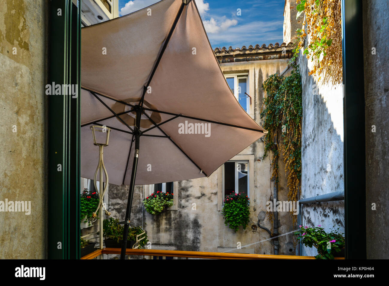 Un piccolo balcone terrazza con un ombrello si apre un cortile con vigneti e fiori su un pomeriggio mediterraneo Foto Stock