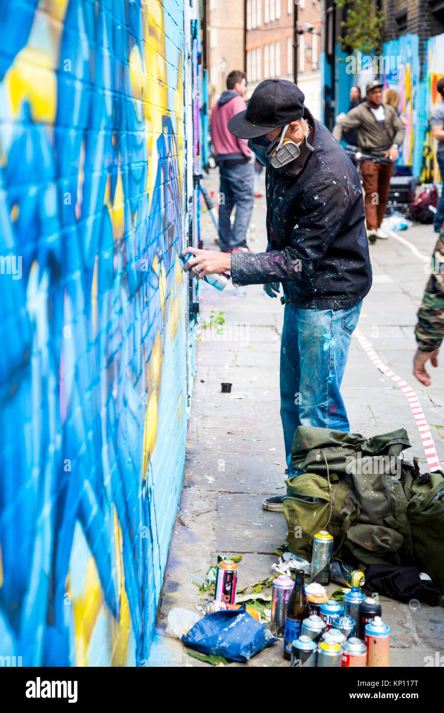 Graffiti artista di strada che indossa una maschera con respiratore spruzzare le pareti in Fleur Street, Londra, Regno Unito Foto Stock