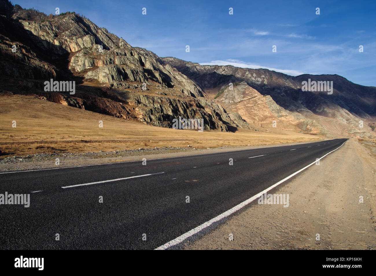 Asfalto stradale percorso su un deserto wild mountain valley giallo erba secca sullo sfondo delle gamme alta sotto un cielo blu Chuysky tratto Altai Mountain Foto Stock