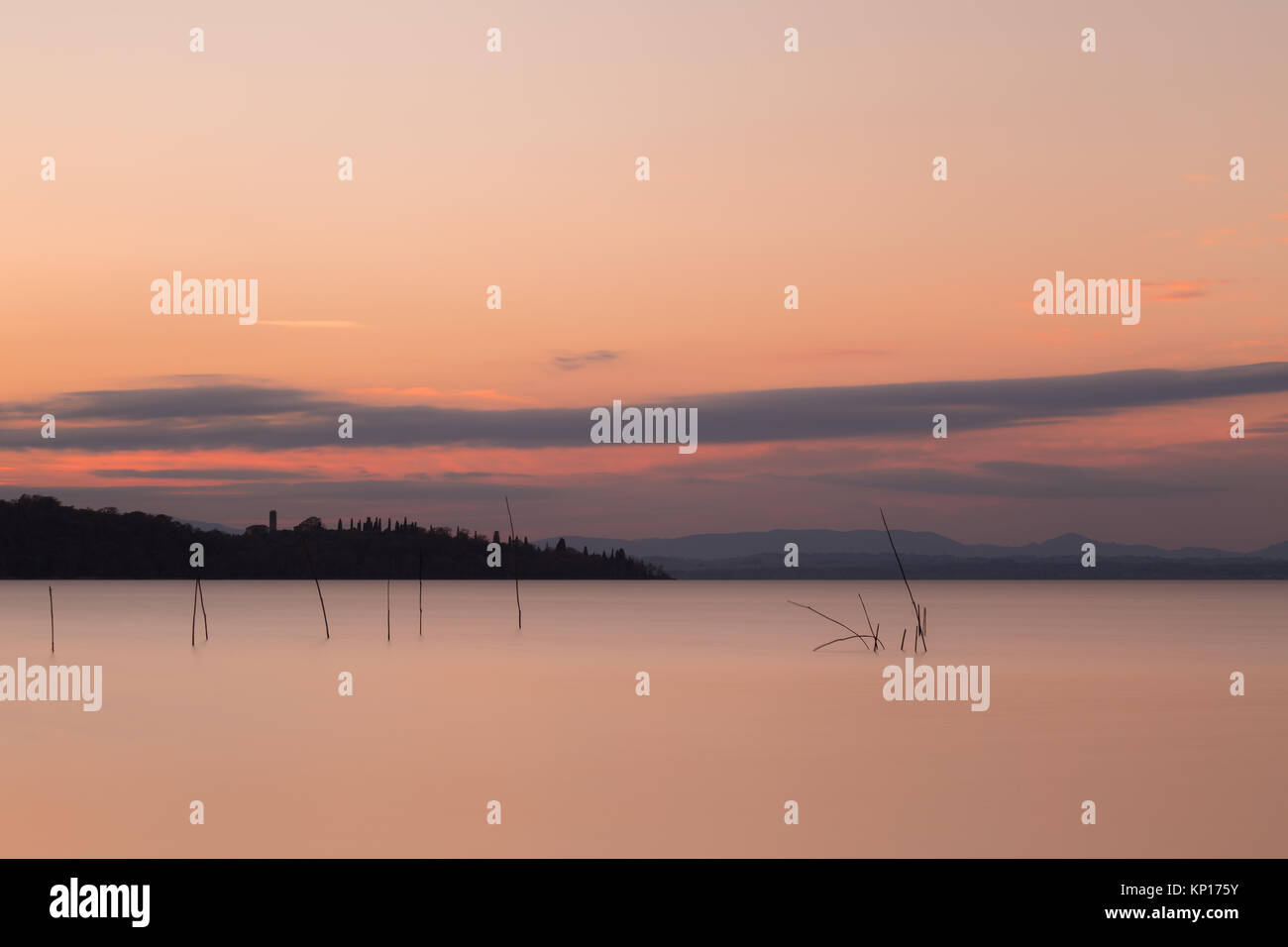 Una lunga esposizione vista del lago Trasimeno (Umbria, Italia) al tramonto, con poli e reti da pesca su perfettamente ancora acqua e un'isola in background Foto Stock