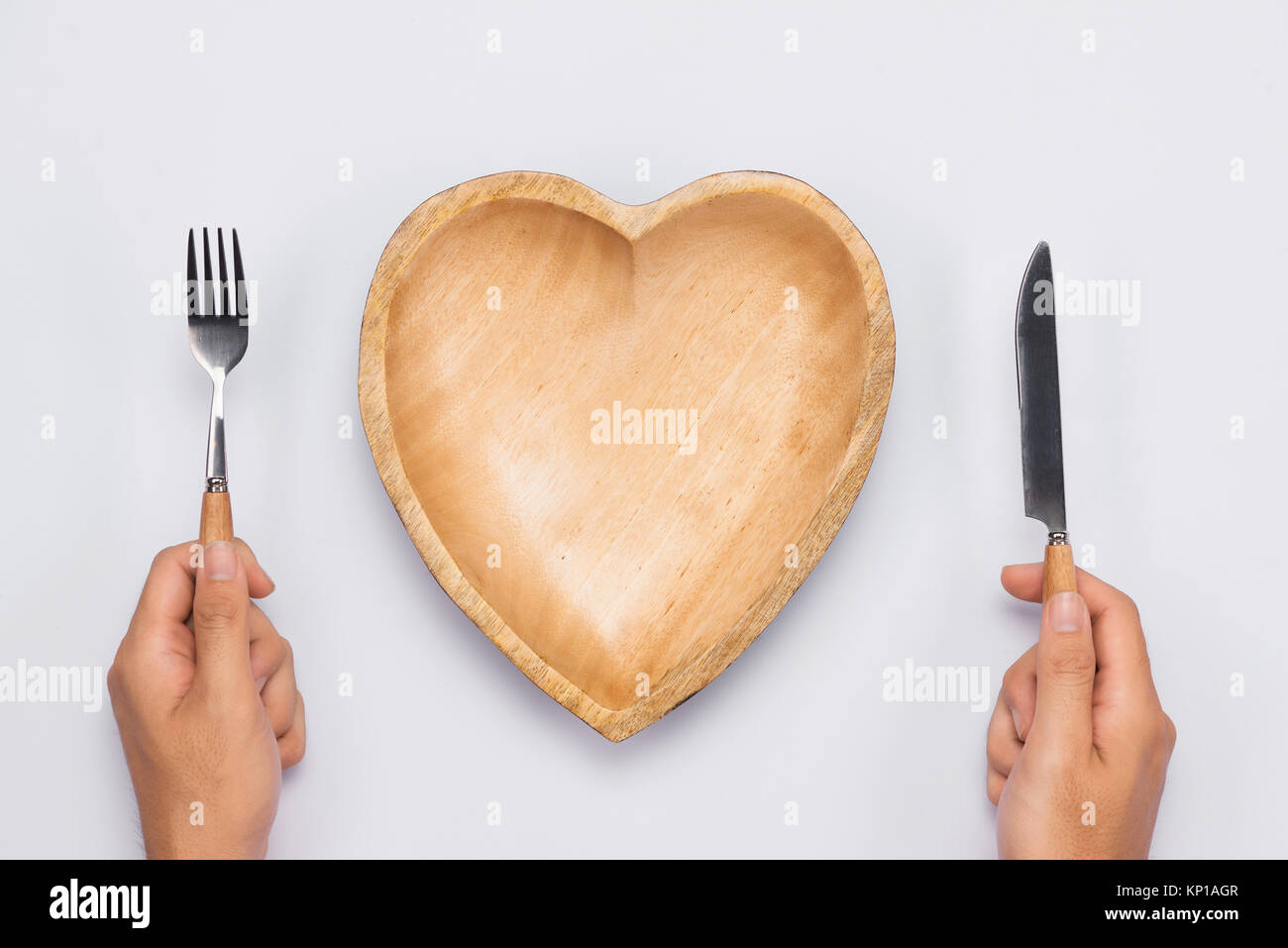 Piatto di legno a forma di cuore, tavola coltello e forchetta in mani. Foto Stock