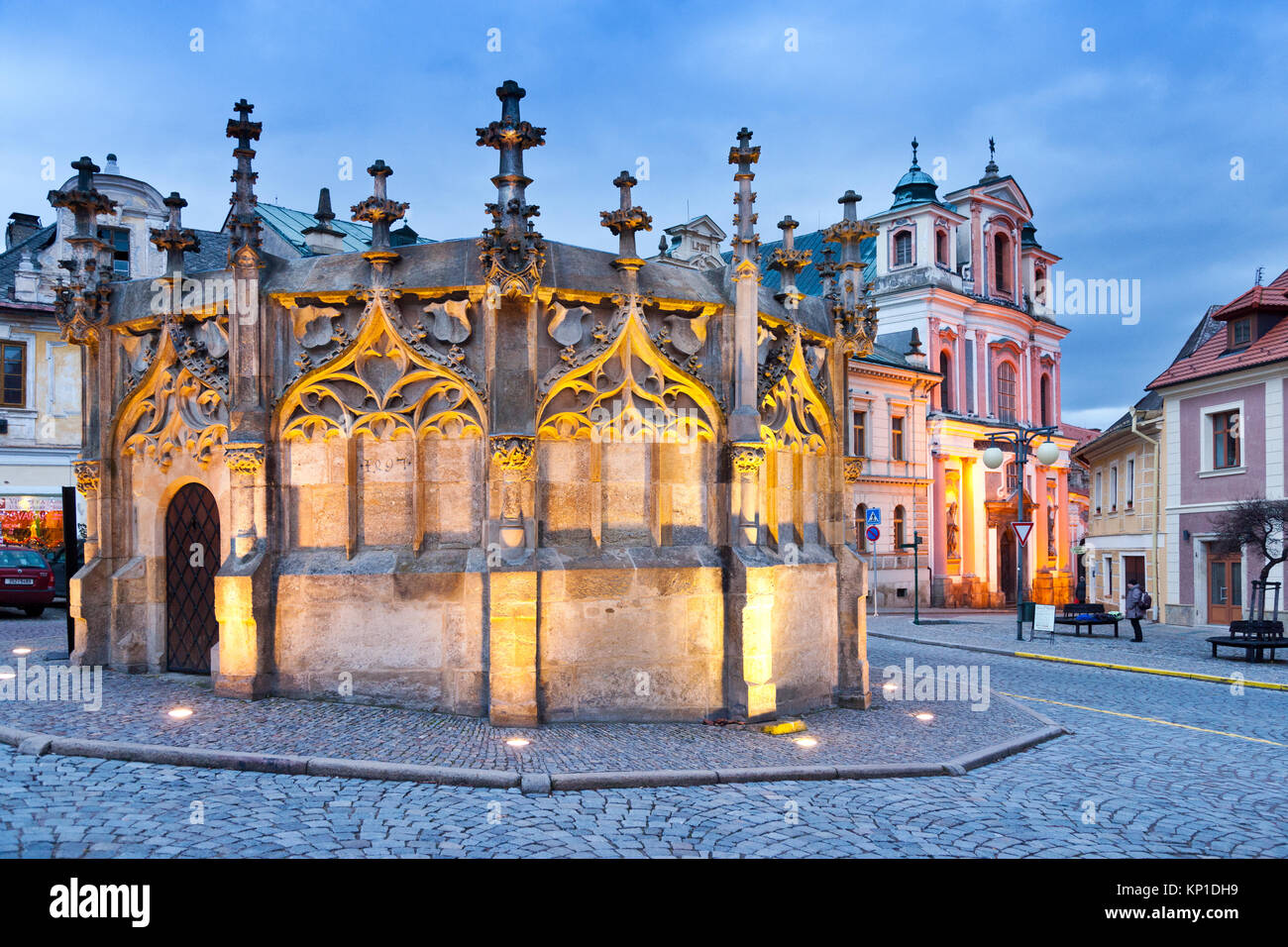 Acqua gotico bene dal 1495 e barocca di San Nepomuk chiesa dal 1734, l'UNESCO, Kutna Hora, Central Bohemia Repubblica Ceca - notte foto Foto Stock