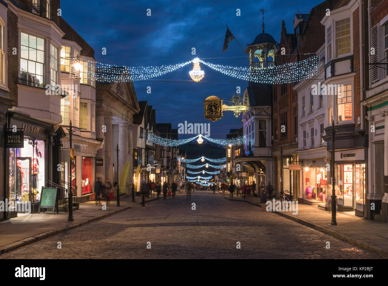 La High Street in Guildford con luci di Natale e la famosa Guildhall orologio in oro in blu ora su una notte tarda giornata di shopping, England Regno Unito Foto Stock