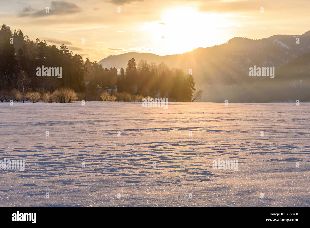 Un pittoresco paesaggio invernale con alberi, montagne e velatura in un congelati lago innevato sotto i raggi del sole all'alba Foto Stock