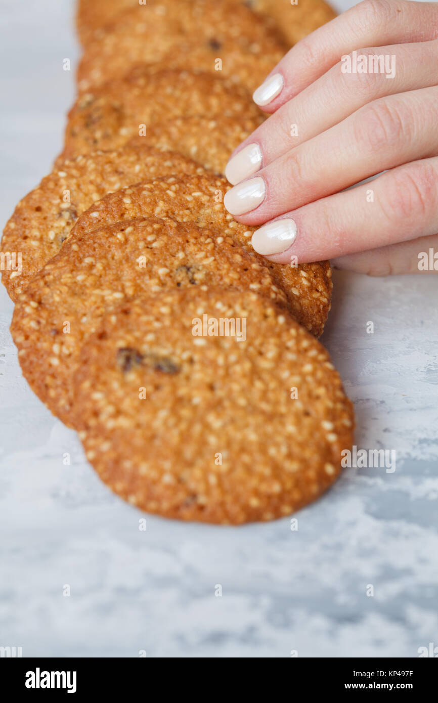 Una donna di mano richiede un round biscotto sani in bianco di sesamo e uvetta. Vegano concetto dessert. Foto Stock Una donna di mano richiede un round biscotto sani in bianco di sesamo e uvetta. Vegano concetto dessert. Foto Stock