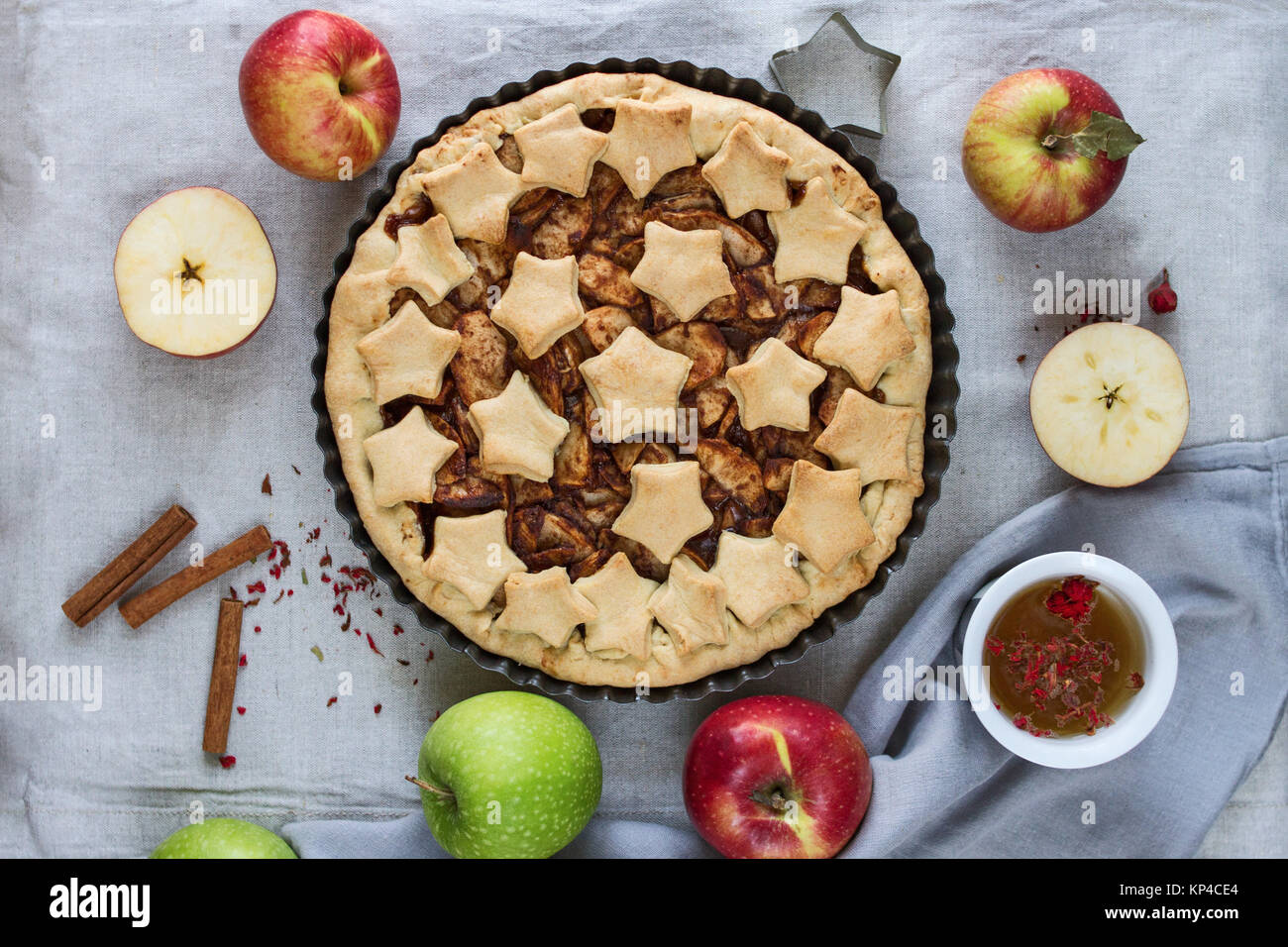 In casa tradizionale American apple pie decorate con stelle in un metallo teglia, il rosso e il verde le mele intere e tagliare, bastoncini di cannella e una tazza. Foto Stock