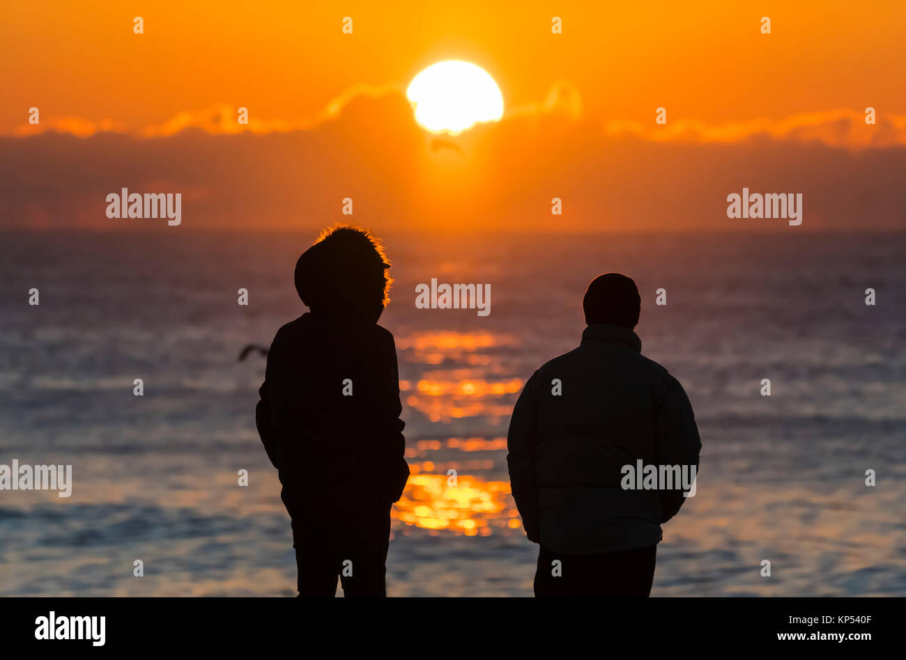 Silhouette di 2 persone in piedi sul mare guardando il sorgere del sole in inverno nel Regno Unito. Foto Stock