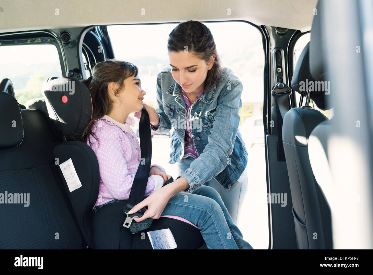 Donna aiutando a sua figlia di allacciare le cinture di sicurezza in auto, la ragazza è seduta su una sicurezza seggiolino da bambino per auto Foto Stock