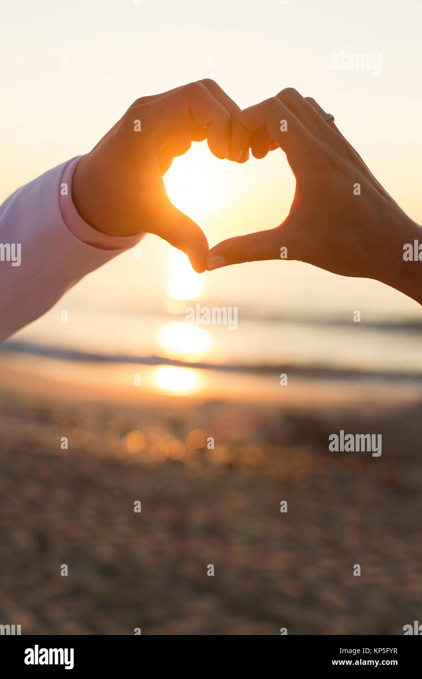 Sonnenaufgang am Strand, Paar formt Herz mit Haenden - tramonto sulla spiaggia, giovane fa un cuore con le mani Foto Stock