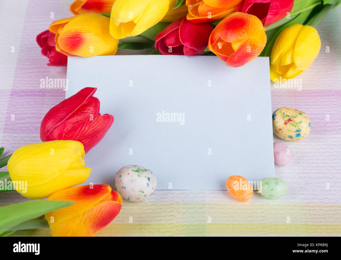 Pasqua candy e tulipani intorno ad una busta vuota su un piano portapaziente colorati Foto Stock