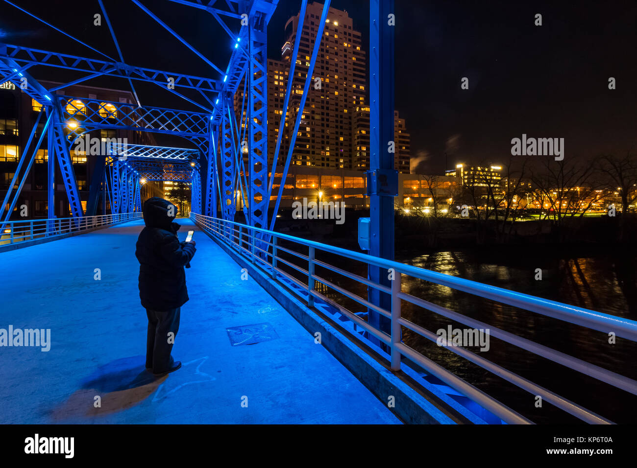 Donna visualizzazione telefono cellulare di notte sul ponte blu sopra il gran fiume in Grand Rapids, Michigan, Stati Uniti d'America Foto Stock