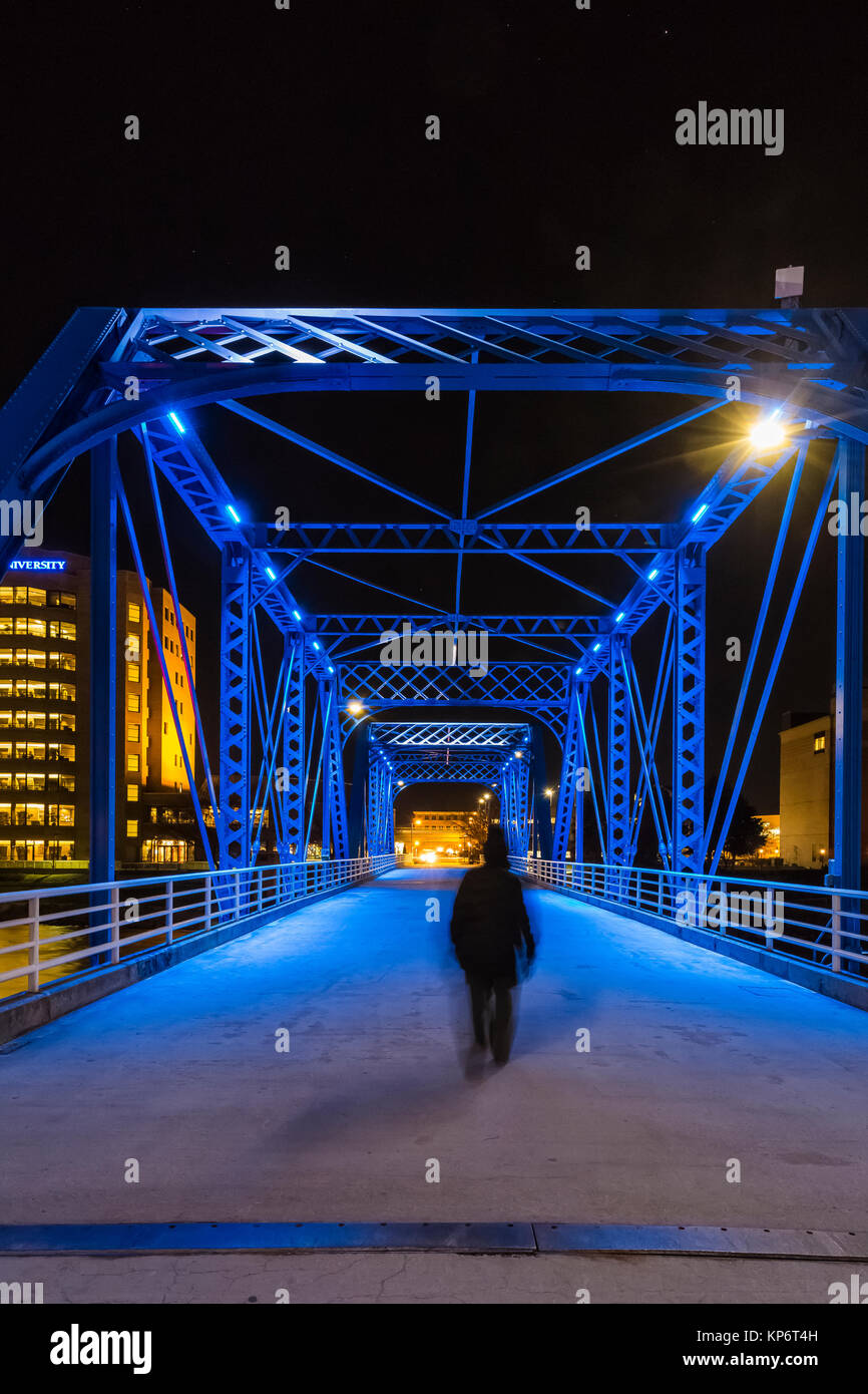La donna a camminare da soli di notte attraverso il ponte blu sopra il gran fiume in Grand Rapids, Michigan, Stati Uniti d'America Foto Stock