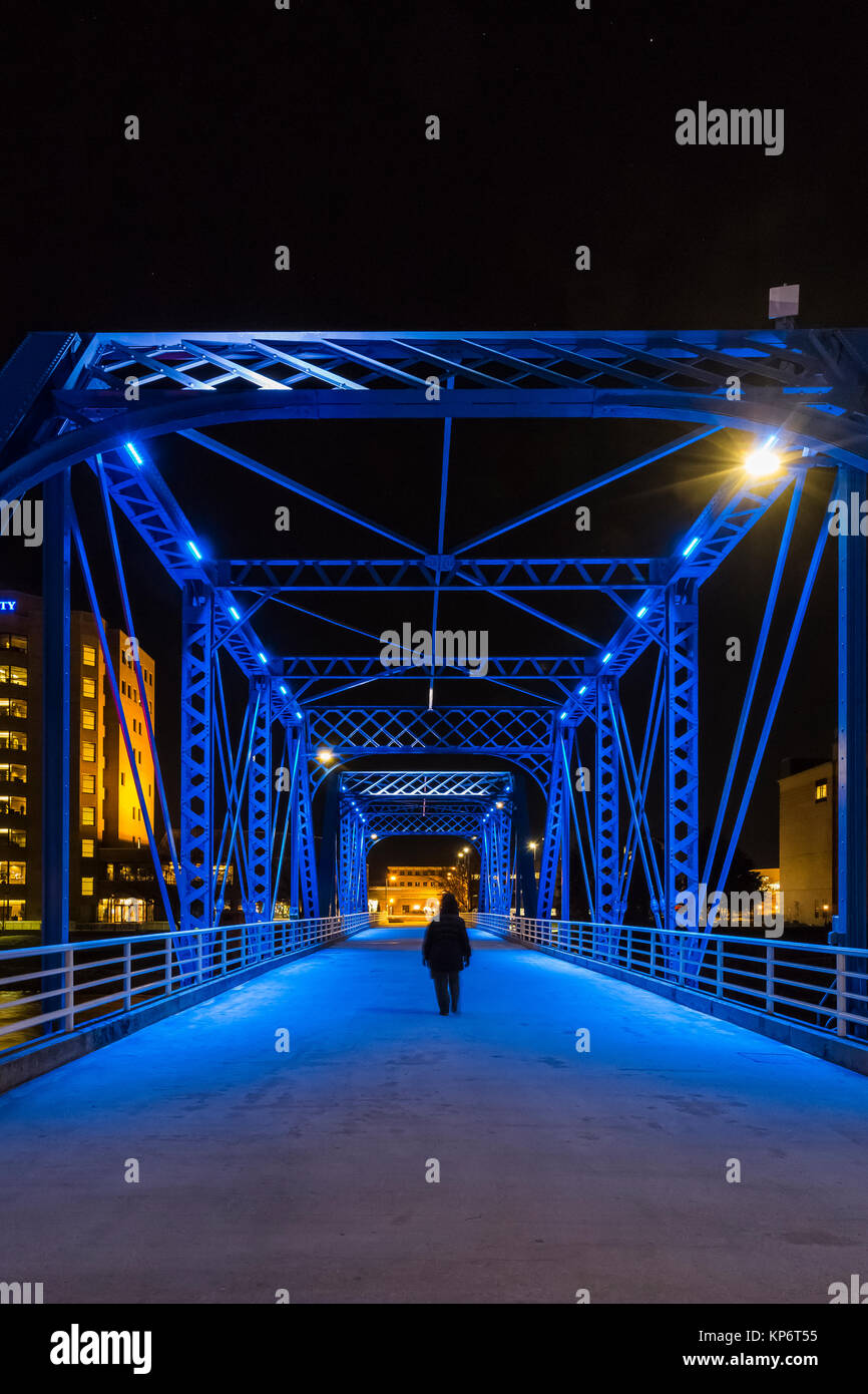 La donna a camminare da soli di notte attraverso il ponte blu sopra il gran fiume in Grand Rapids, Michigan, Stati Uniti d'America Foto Stock