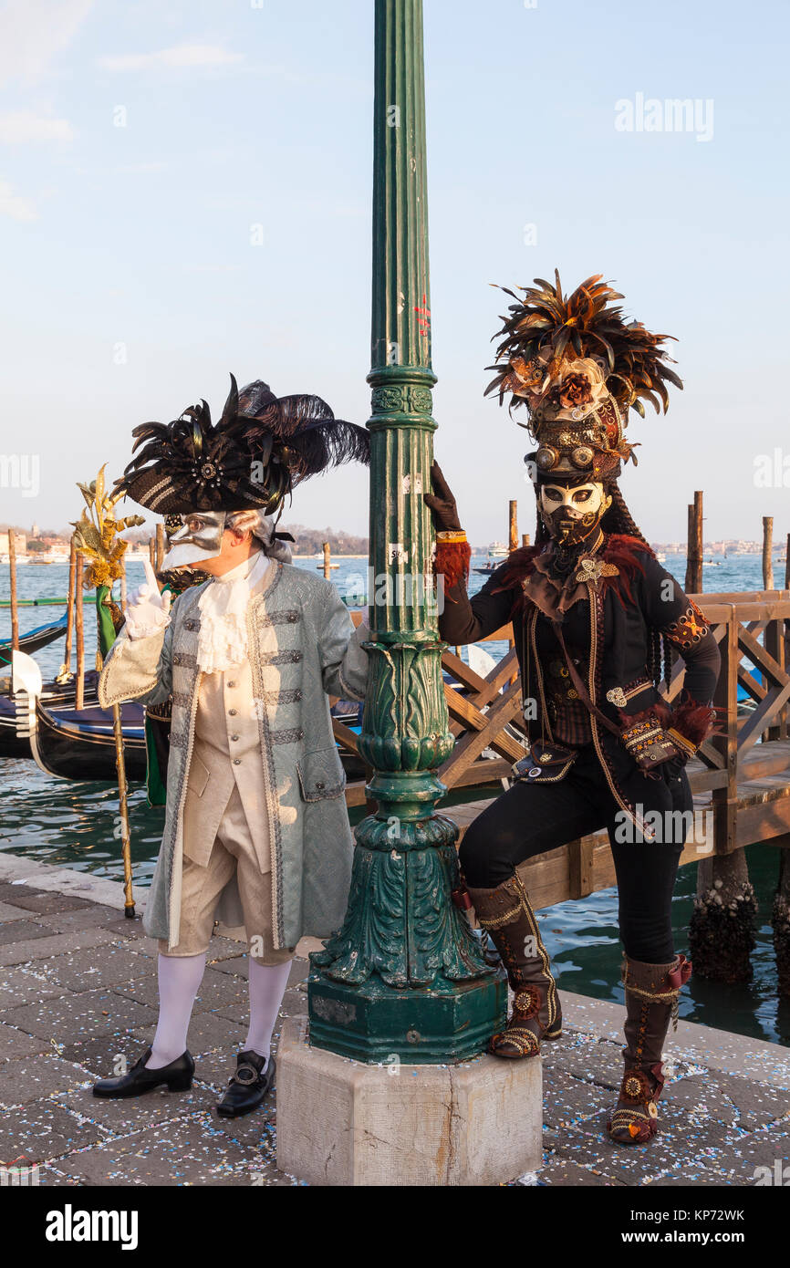 2017 Carnevale di Venezia, Venezia, Veneto, Italia, due persone in costume che pongono presso la laguna al tramonto con gondole Foto Stock