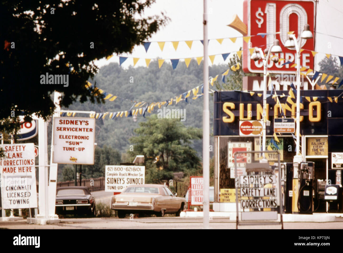 Una delle diverse stazioni di servizio che pubblicizza Tuneups per passare le emissioni e i test di sicurezza si trova vicino a una emissione automatica stazione di ispezione nel centro cittadino di Cincinnati, Ohio...Agosto 1975 Foto Stock