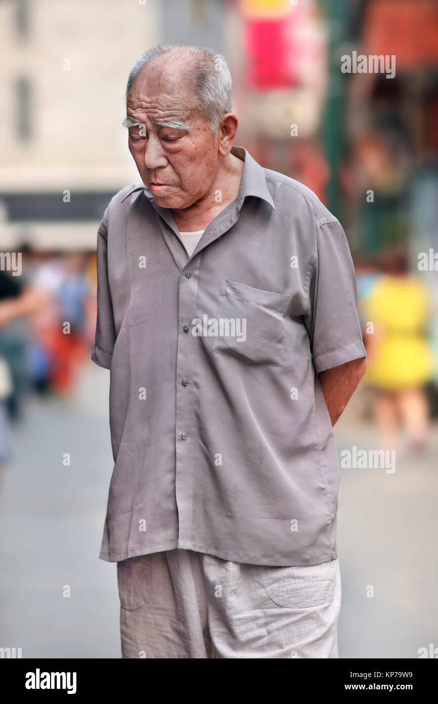 Pechino-Giugno 9, 2015. Ritratto di un vecchio vestito estivo uomo cinese che ha perso in mente, in piedi in una trafficata via dello shopping nel centro di Pechino. Foto Stock